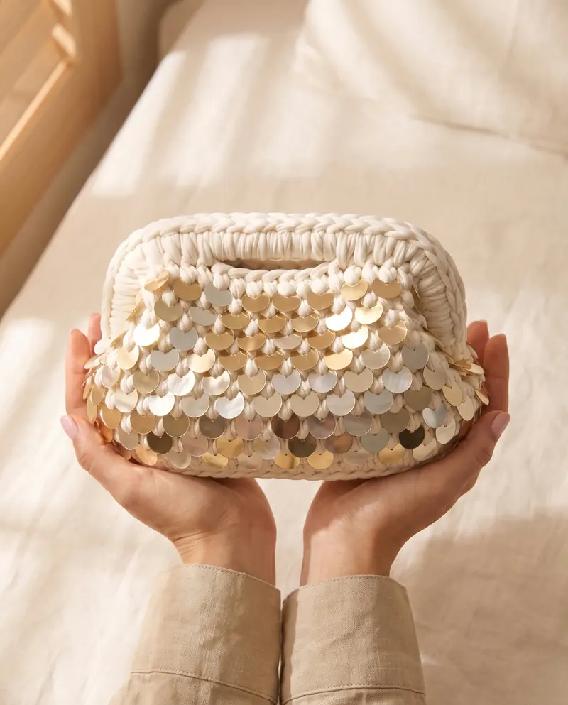 Clutch bianca con paillettes dorate sollevata fra le mani