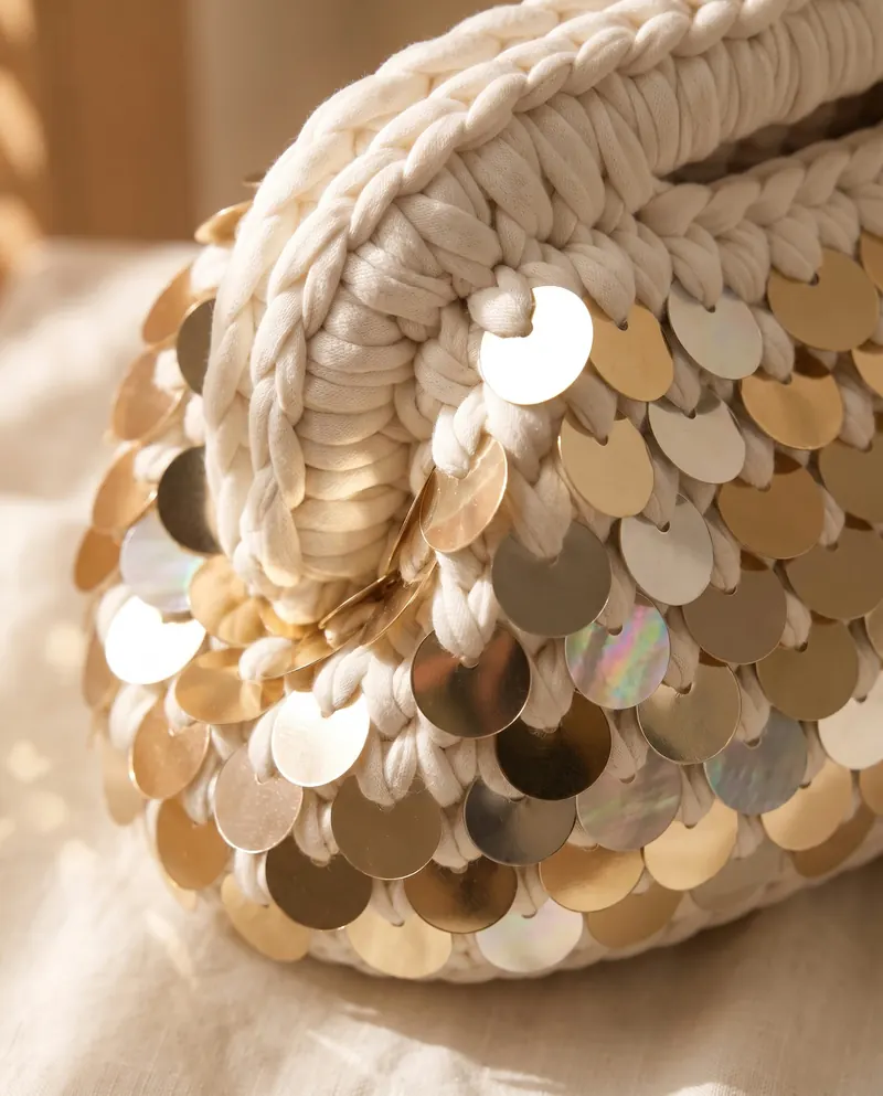 Dettaglio delle grandi paillettes dorate sulla clutch bianca