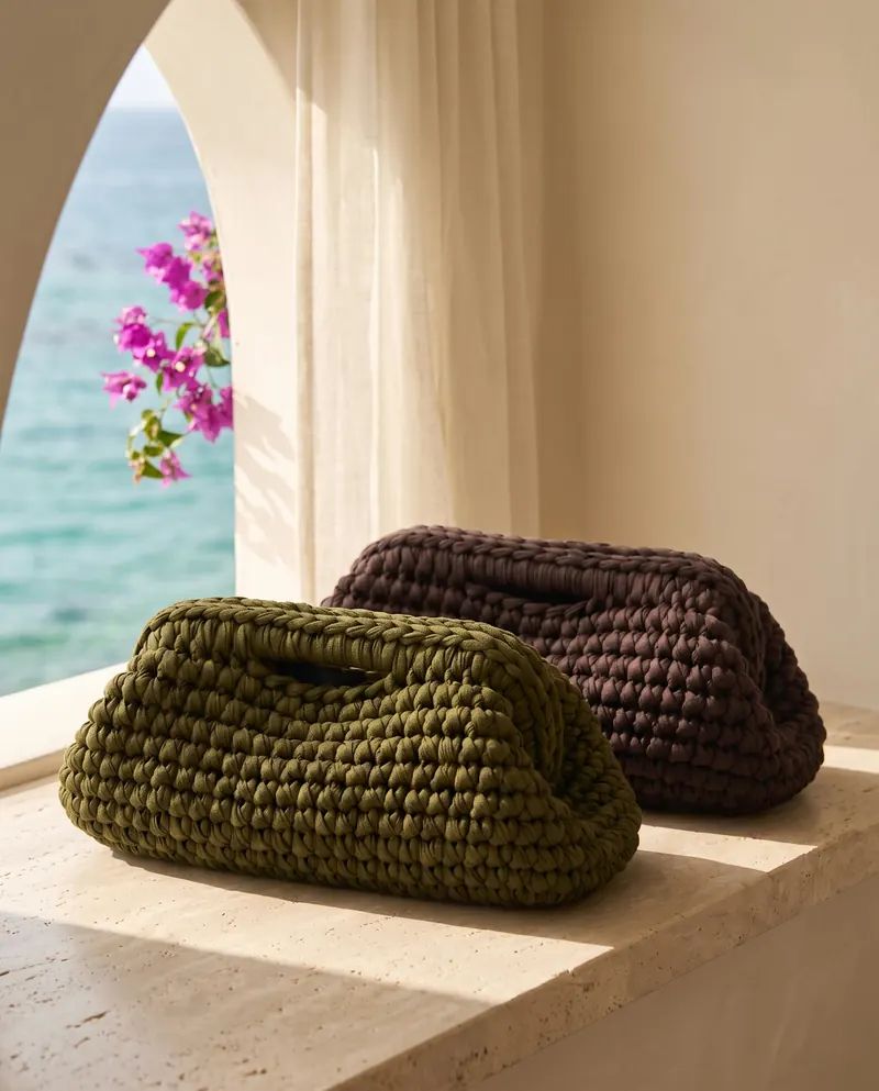 Due clutch a rotolo all'uncinetto, verde oliva e marrone, su un davanzale ad arco sul mare