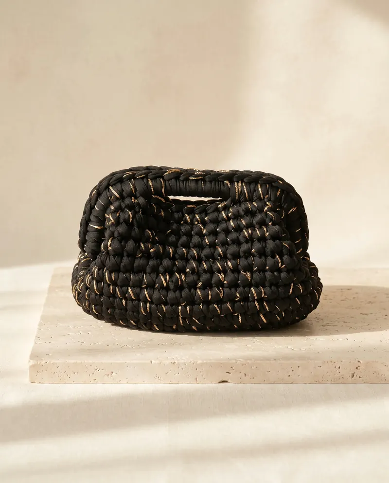 Clutch nera con filo dorato posata su un tavolo chiaro