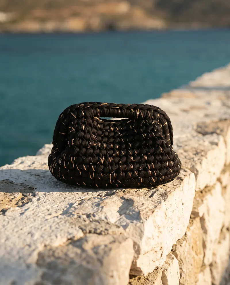 Clutch nera con filo dorato su un muretto di pietra davanti al mare