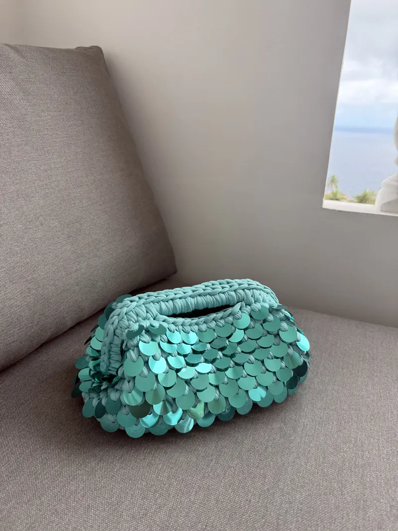 Clutch turchese all'uncinetto con maxi paillettes appoggiata su un divano